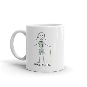 May include: White ceramic mug featuring a black stick figure illustration of a person hiking. The person is wearing a backpack, shorts, and carrying a walking stick. The text "HIKER GIRL" is printed below the illustration.