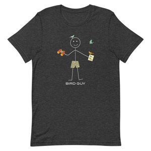 May include: Dark gray t-shirt featuring a stick figure of a person holding binoculars and a bird guide, with birds flying around. The stick figure is wearing patterned shorts. The text "BIRD GUY" is printed below the figure.