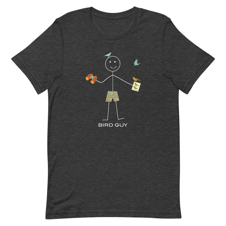 May include: Dark gray t-shirt featuring a stick figure of a person holding binoculars and a bird guide, with birds flying around. The stick figure is wearing patterned shorts. The text "BIRD GUY" is printed below the figure.
