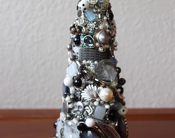 May include: A decorative Christmas tree made from various jewelry pieces. The tree is adorned with pearls, beads, and silver-toned embellishments. A silver filigree topper sits at the top. The tree is approximately 8 inches tall.