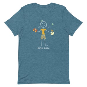 May include: A teal blue t-shirt with a stick figure illustration of a person holding binoculars and a bird identification book. The text "BIRD GIRL" is printed below the illustration.