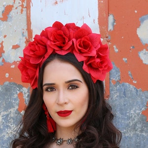 Puede incluir: Una mujer con una diadema floral roja y un vestido negro con estampado floral rojo y rosa. Ella sostiene una sola rosa roja.