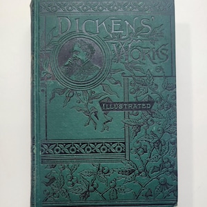 May include: A vintage green book titled "Dickens' Works Illustrated." The cover features a portrait of a man and decorative floral and geometric patterns. The book's spine is also green.