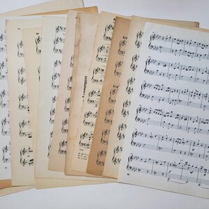 May include: A stack of vintage sheet music with musical notes printed on the pages. The pages are yellowed with age and have a worn, antique look.