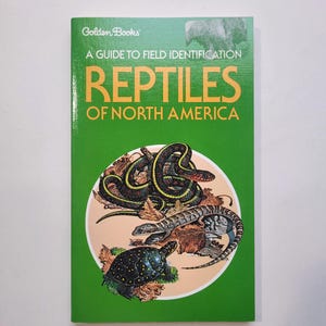 May include: A green Golden Books guide titled "Reptiles of North America." The cover features illustrations of various reptiles, including snakes, a lizard, and a turtle, set against a beige circle. The book's title is in large orange letters.