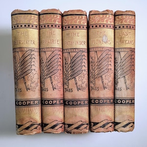 May include: Five vintage hardcover books by Cooper titled The Deerslayer, The Prairie, The Pathfinder, The Pioneers, and The Last of the Mohicans. Each tan spine features gold lettering, a feather illustration, and the text Leatherstocking Tales.