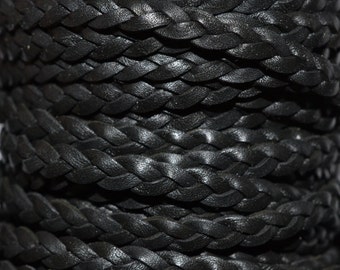 May include: Close-up of a tightly wound spool of black braided cord. The cord is made of a smooth, possibly leather-like material, with a consistent, dark color. The braid pattern is clearly visible, creating a textured surface.