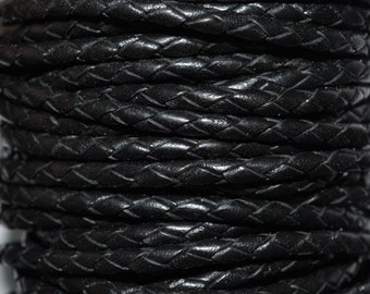 May include: Close-up of a spool of black braided leather cord. The cord is tightly wound and has a smooth, polished finish.