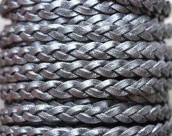 May include: Close-up of a silver braided leather cord. The cord is made of multiple strands of leather that are woven together to create a braided effect. The cord is smooth and shiny, and it has a metallic sheen.