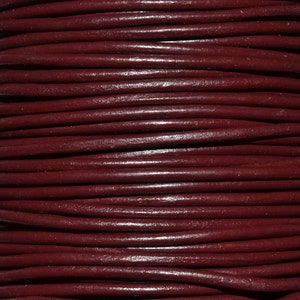 May include: Close-up of a spool of dark red leather cord. The cord is smooth and shiny, and it is wound tightly around the spool.