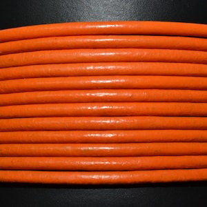 May include: Close-up of a spool of bright orange leather cord. The cord is smooth and has a slight sheen.