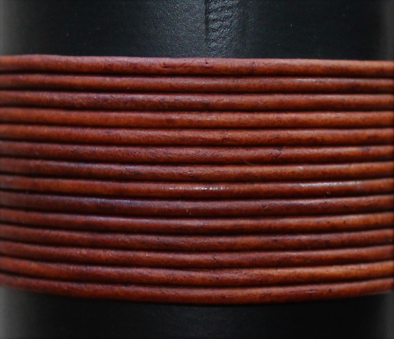 May include: Close-up of a brown leather cord wrapped around a black surface. The cord is made of multiple strands of leather, creating a textured look.