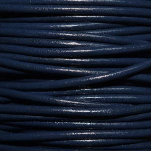 May include: A close-up of a spool of dark blue leather cord. The cord is tightly wound and has a smooth, polished finish.