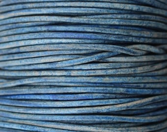 May include: A close-up of a spool of blue leather cord. The cord is tightly wound and has a slightly distressed look.