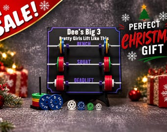 Puede incluir: Un tablero de exhibición rectangular negro con el texto Dee's Big 3 Pretty Girls Lift Like This, tres barras horizontales con discos de pesas en miniatura etiquetados como Bench, Squat y Deadlift, junto a discos de pesas sueltos.
