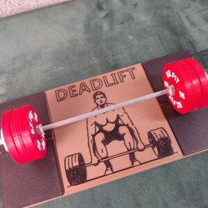 May include: A red and white weightlifting set with a barbell and two weight plates. The set is on a brown surface with the word "DEADLIFT" printed on it. A black and white illustration of a person lifting weights is also on the surface.