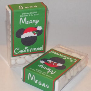 May include: Two clear plastic containers filled with white mints. Each container has a green, red, and black label with a Mickey Mouse head wearing a Santa hat. The labels read "Merry Christmas!" and include the names "John" and "Megan".