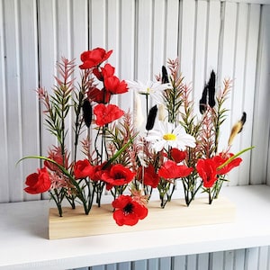 Puede incluir: Un arreglo floral de madera con amapolas rojas y margaritas blancas. Las flores están dispuestas en una base de madera con un acabado de madera natural.