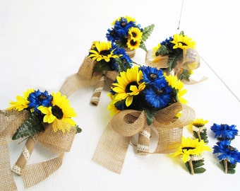 May include: A set of six bouquets featuring yellow sunflowers and blue cornflowers, tied with hessian ribbon. The bouquets are arranged on a white surface.