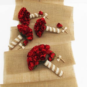 May include: Four red rose bouquets with white and cream ribbon accents on a hessian background.