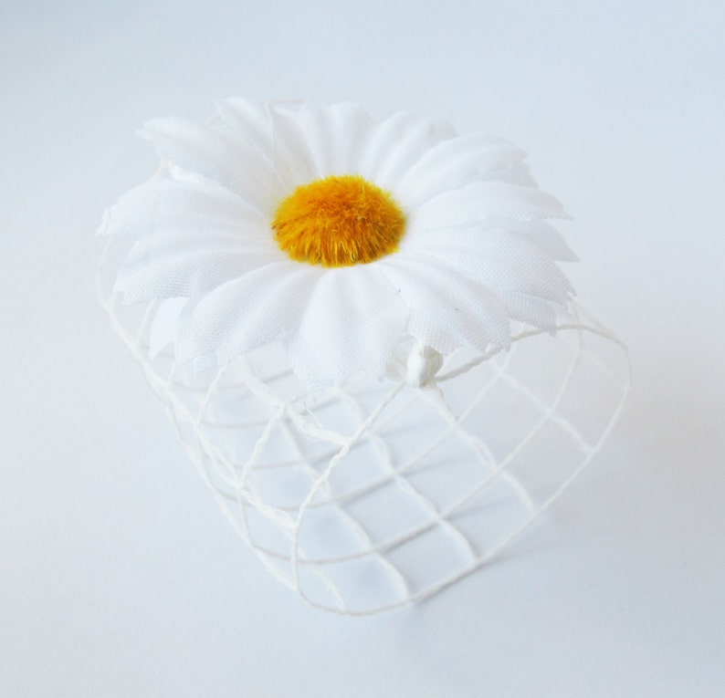 May include: A white daisy with a yellow centre is placed inside a white wire mesh basket.