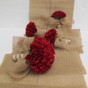 May include: Three bouquets of red roses wrapped in hessian fabric. The bouquets are tied with white ribbon and are arranged on a hessian surface.