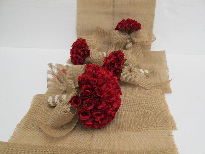 May include: Three bouquets of red roses wrapped in hessian fabric. The bouquets are tied with white ribbon and are arranged on a hessian surface.