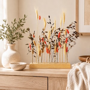 Peut inclure: Composition florale décorative avec du blé séché, des accents rouges et bruns. L'arrangement est placé dans une base en bois clair. Un vase avec de la verdure et un petit bol sont également visibles.