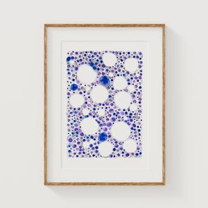May include: Abstract art print in a wooden frame. The artwork features a pattern of white and blue circles and dots on a white background. The artwork is framed with a light brown wooden frame and is displayed on a white wall.