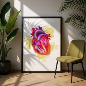 May include: A framed print featuring a vibrant, anatomical illustration of a human heart. The heart is rendered in shades of red, pink, and purple, set against a white background with yellow paint splatters. The artwork is displayed in a black frame.