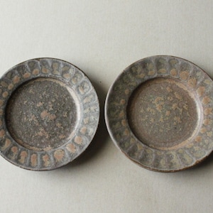 Peut inclure: Deux assiettes en céramique avec un glaçage moucheté brun et gris. Les assiettes ont un motif décoratif autour du bord.