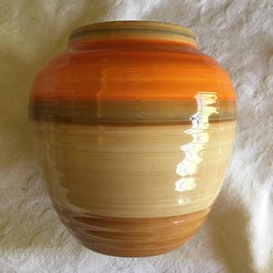 May include: A ceramic vase with a striped design in shades of orange, brown, and beige.