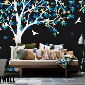 May include: A white tree silhouette with blue, green, and yellow leaves and small white birds on a black background. A couch with pillows and a throw blanket is in the foreground. The text "ON WALL Studio" is in the bottom left corner.