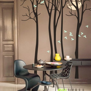 May include: Black and white silhouette wall decal of trees with birds flying around them. The decal is on a brown wall with a black table and chairs in front of it.