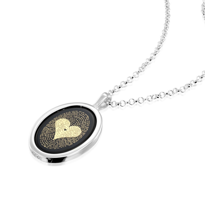 A silver necklace with an oval pendant. The pendant has a black background with a gold heart design. The heart is made up of tiny words. The necklace is on a white background.