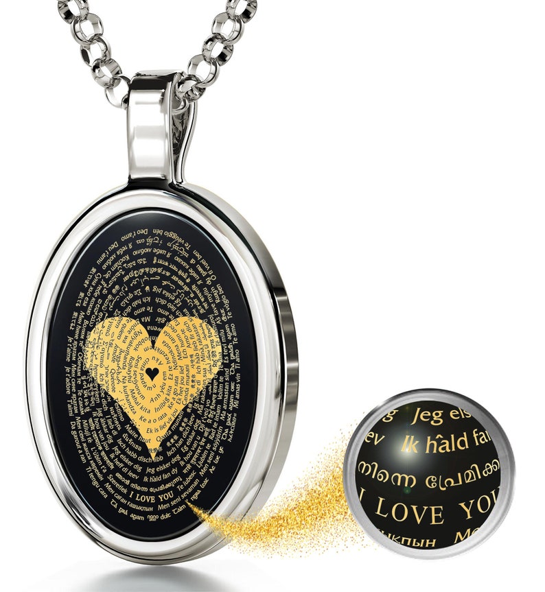 A silver oval pendant necklace with a black background and a gold heart design. The heart is made up of the word 'I love you' written in multiple languages. The pendant is on a silver chain. The necklace is a romantic gift for a loved one.