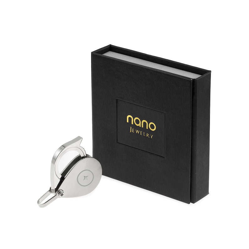A silver-colored ring with a small, round, clear stone in the center. The ring is on a white surface and is next to a black box with the words 'nano JEWELRY' in gold lettering.
