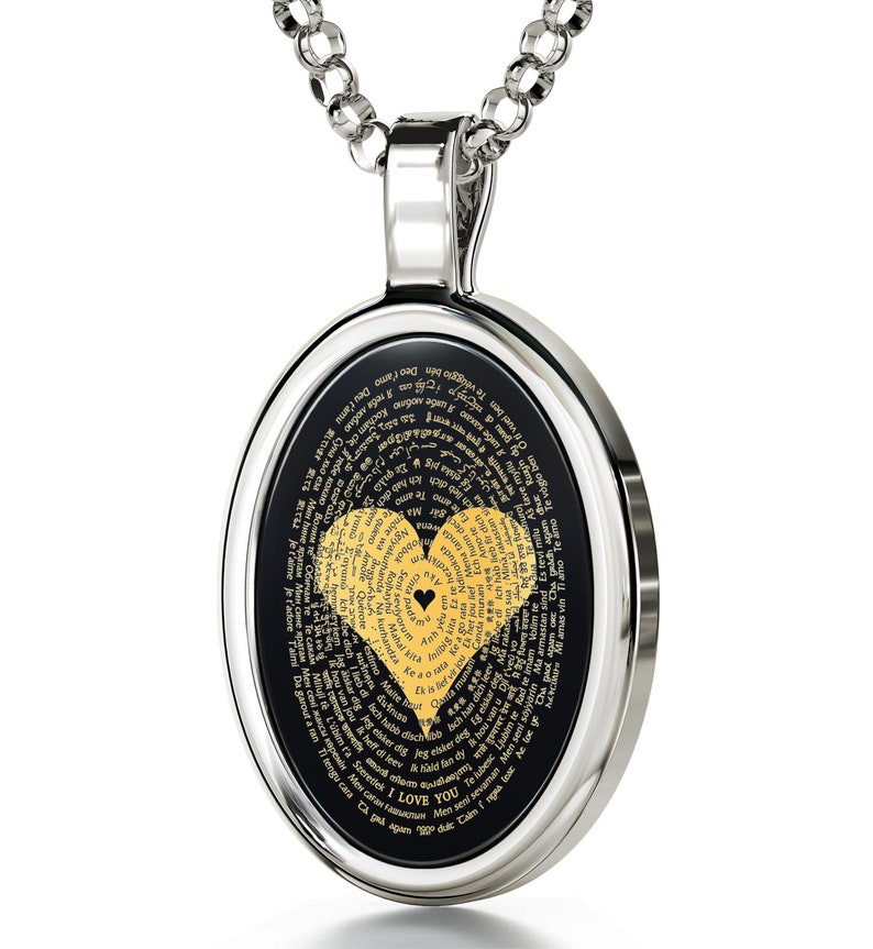 A silver oval pendant necklace with a black background and a gold heart design. The heart is made up of words in different languages that say 'I love you.' The words are arranged in a spiral pattern around the heart.