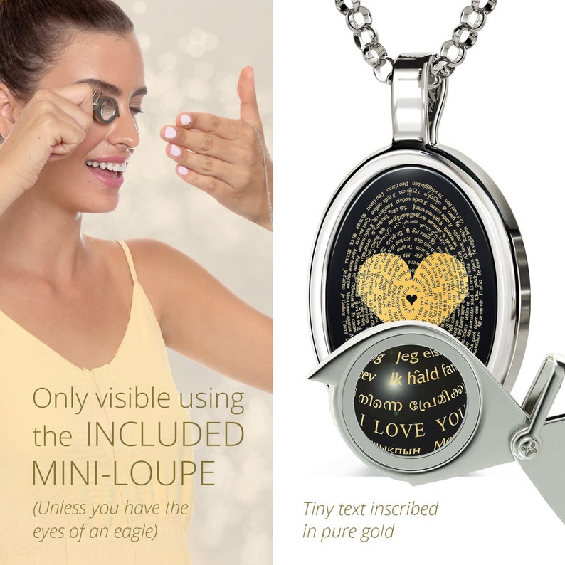 A silver necklace with a round pendant. The pendant has a black background with a gold heart design. The heart is inscribed with the words 'I love you' in multiple languages. The pendant is attached to a silver chain. The pendant is shown with a magnifying glass to show the small inscription.