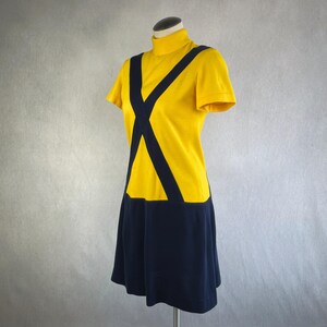 May include: A short-sleeved dress featuring a bright yellow bodice with a high mock neck collar and a dark navy blue skirt. Two thick dark navy blue bands cross diagonally over the chest, connecting the bodice to the solid navy blue skirt section.