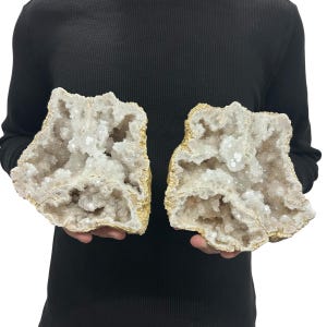 May include: Two large, matching halves of a geode featuring a rough, tan-colored exterior and a hollow interior filled with sparkling, translucent white and pale beige crystalline structures. The mineral specimens have irregular, jagged edges.