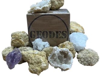 Könnte beinhalten: Eine Holzkiste mit der Aufschrift "GEODES" mit verschiedenen Geodenkristallen darin. Die Kristalle sind in verschiedenen Schattierungen von Weiß, Braun und Lila.