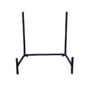 May include: Black metal display stand with a simple design. The stand has two vertical supports and a horizontal base with two small feet on each side.