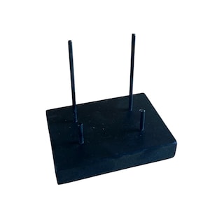 May include: A black display stand with a rectangular base and four vertical rods. The rods are of varying heights, and the stand is likely used for displaying small items or jewelry. The stand is made of a solid, dark material.