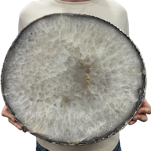 May include: A large, round agate slab with a polished surface. The natural stone features a white and gray color palette with intricate patterns and a dark gray edge. This decorative piece is ideal for home decor.