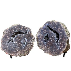 May include: Two large, round, gray and brown geode halves with a white crystal interior. The geode halves are on black metal stands.
