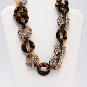 May include: A brown and gold necklace with large, round links. The links are made of a tortoiseshell-patterned material and are accented with clear rhinestones.