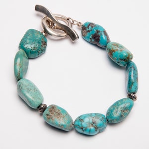 May include: A turquoise gemstone bracelet with a silver toggle clasp. The bracelet features a series of smooth, oval-shaped turquoise stones.