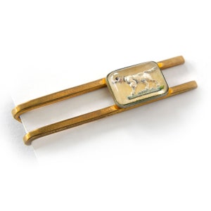 May include: A gold tie bar with a rectangular glass inset featuring a white dog illustration.