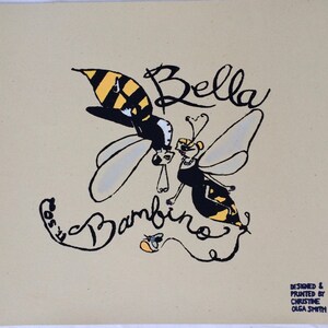 Peut inclure: Une illustration d'abeille noire et jaune avec le texte "Bella Bambinos" en cursive noire. L'abeille porte un smoking et un nœud papillon. Le texte "Designed & Printed by Christine Olga Smith" et "Blue Fig Arts" se trouve dans le coin inférieur droit.
